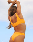 Side view of a female swimmer wearing a JAYD Swimwear Cali bikini bottom in Sunshine Yellow against a blue sky.