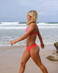 Side view of model walking in athletic, cheeky coverage JAYD Swimwear Minnie bikini bottoms in fiesta.