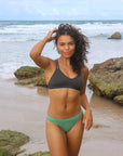 Front view of model on a beach wearing JAYD Swimwear athletic Tazzie training bikini top in Carbon.