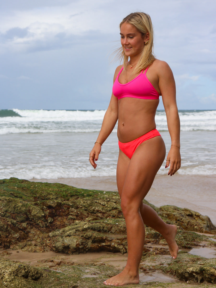 Front view of model walking in JAYD Swimwear athletic Tazzie training bikini top in Pink Sorbet.