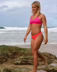 Front view of model walking in JAYD Swimwear athletic Tazzie training bikini top in Pink Sorbet.