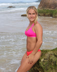 Side view of model sitting on a rock wearing JAYD Swimwear athletic Tazzie training bikini top in Pink Sorbet.