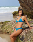 Front view of model sitting on a rock wearing JAYD Swimwear athletic Triangle training bikini top in Nordic Blue.