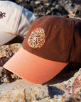 JAYD Swimwear Brown & Apricot Baseball Cap sitting on a rock.