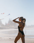 Woman in a Cacao brown JAYD chlorine resistant swimsuit on a beach with kites in the background