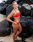 Surf Lifesaving athlete Emma Woods in the Torquay Ruby Bikini Top on the beach with rocky landscape in the background.