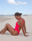 JAYD Swimwear, athletic one piece, Finley in the Fiesta colour. Side seated image one the beach.