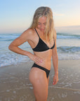 Side view of seamless, athletic, cheeky coverage JAYD Swimwear Minnie bikini bottoms in Black.