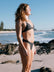 Woman in a Carbon grey bikini standing on a beach with ocean and sky in the background. She wears the Triangle top and Cali bottom