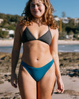 Woman wearing a Carbon coloured JAYD bikini top and Nordic blue full coverage bottoms on a beach.