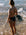 Brodee wears the Tallow One Piece in Carbon grey, walking along a beach with waves.