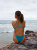 JAYD Swimwear, Zimmy one piece in Atlantic, view of the back of the suit, seated on the rocks.