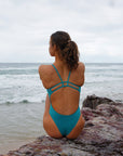 JAYD Swimwear, Zimmy one piece in Atlantic, view of the back of the suit, seated on the rocks.