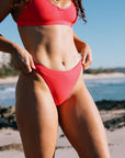 Person wearing JAYD Fiesta bikini bottom called Cali on a beach with ocean and sky in the background