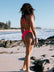 Madi wears a Fiesta bikini bottom offering mid coverage, called Cali, standing on a beach with ocean and sky in the background