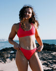 Madi in a Fiesta, mid-coverage bikini bottoms, called Cali. Standing on a beach with ocean in the background.