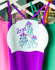 Three jellyfish flower illustrations on a white swim cap with pink, purple and green swimsuits in the background.