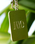 Back of JAYD Swimwear shell stamp keyring, featuring embossed JAYD lettering, hanging on a branch.