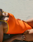 JAYD Swimwear Lennox one piece in flare orange with contrasting ignite yellow straps boldly popping against a beige sandy background.
