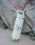 JAYD Swimwear mint green water bottle leaning against a rock at the beach.