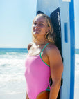 Surf life saving athlete Emily Doyle standing on the beach with a blue board in the JAYD Swimwear Zambia Fairy Floss x Meadow one piece swimsuit.