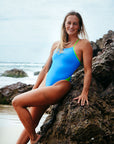 Surf life saving athlete Liv Corrin leaning against a rock at the beack wearing the vibrant Zambia Cancun x Splice Jaye one piece swimsuit.