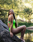 JAYD model Jenaya sitting on a rock next to a creek in the vibrant Zambia Splice one piece with contrasting Cancun shoulder straps.