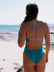Woman in an Atlantic coloured JAYD one piece standing on a beach with ocean view. She is wearing the Airlie one piece