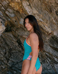 Woman in a Atlantic coloured lennox one piece standing against a stone wall