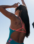 Woman wearing Lennox one piece swimsuit against a clear blue sky. She is wearing the colour Atlantic