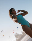 Madi wears the Ibiza One Piece in Mykonos blue, with contrasting hip cutouts in Sunshine and Lilac Haze, made from chlorine resistant fabric.