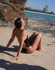 Woman in a JAYD contrasting swimsuit sitting on a beach with ocean and cliffs in the background