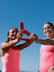 Two women in vibe coloured swimsuits holding red popsicles against a clear blue sky. Both girls are wearing JAYD fixed back one pieces.