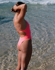 Woman in a JAYD, Vibe coloured Tallow one piece, standing in shallow water near the ocean.
