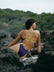JAYD Swimwear model sitting on a rocky beach in the Lennex contrast one piece in Acai purple and daffodil yellow.