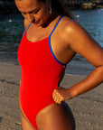 Athlete Pipi Te Pania wearing the Airlie one piece swimsuit in Ruby with contrasting cobalt shoulder straps in a sunny beach.