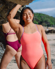 Surf life saving athlete Sara standing on a rocky beach wearing the JAYD Swimwear Airlie one piece in vibe with lilac haze shoulder straps.
