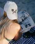 JAYD model laying on the beach reading a magazine wearing the cream JAYD baseball cap.