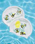 Two white swim caps with yellow and black bumblebee illustrations and the words 'JAYD SWIMWEAR' and 'BEE HAPPY', floating on blue water.