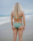 JAYD Swimwear model standing on a beach looking into the distance showcasing the full coverage fit of the Connie Matcha bottoms.