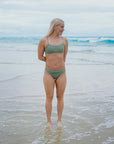 Olympic swimmer Ella Ramsay standing on a beach with the ocean behind her, wearing the JAYD Swimwear Connie Matcha Bottoms and matching Torquay Top.