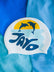 White swim cap with dolphins jumping out of the water and 'JAYD' branding on a blue swimsuit background