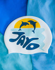 White swim cap with dolphins jumping out of the water and 'JAYD' branding on a blue swimsuit background