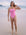 JAYD Swimwear athlete Jenaya Massie standing on a beach wearing the Airlie one piece swimsuit in Fairy Floss pink with contrasting Flare orange shoulder straps.