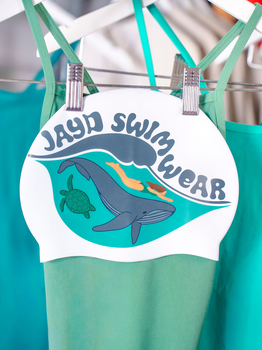 Swim cap design with woman diving above a whale and turtle, & JAYD Swimwear text above wave.
