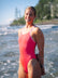 JAYD Swimwear athlete Claudia Slaven standing on a beach wearing the Finley one piece swimsuit in fiesta with contrasting fairy floss pink shoulder straps.