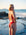 JAYD athlete Mia Cook standing on a rocky beach looking over her shoulder wearing the Finley one piece swimsuit in Ruby red.