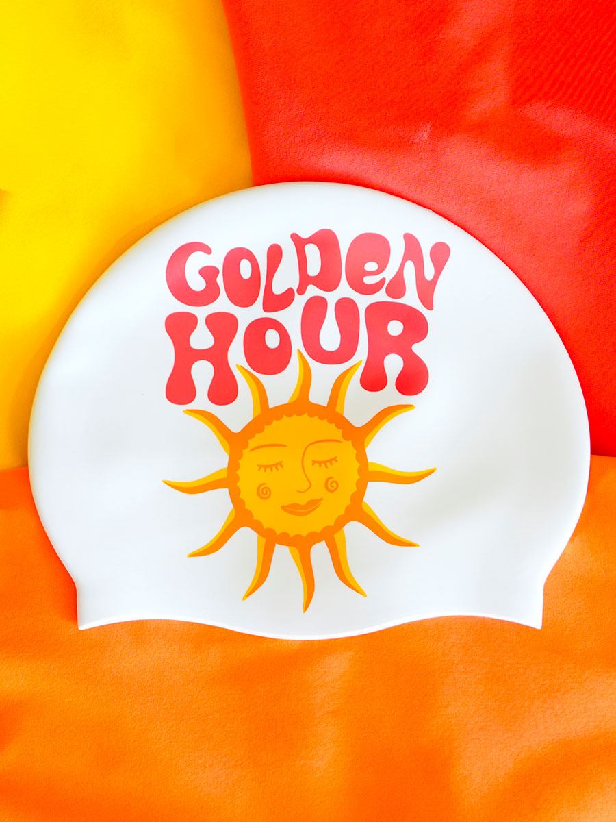 White swim cap with 'Golden Hour' text and sun illustration on a colorful background