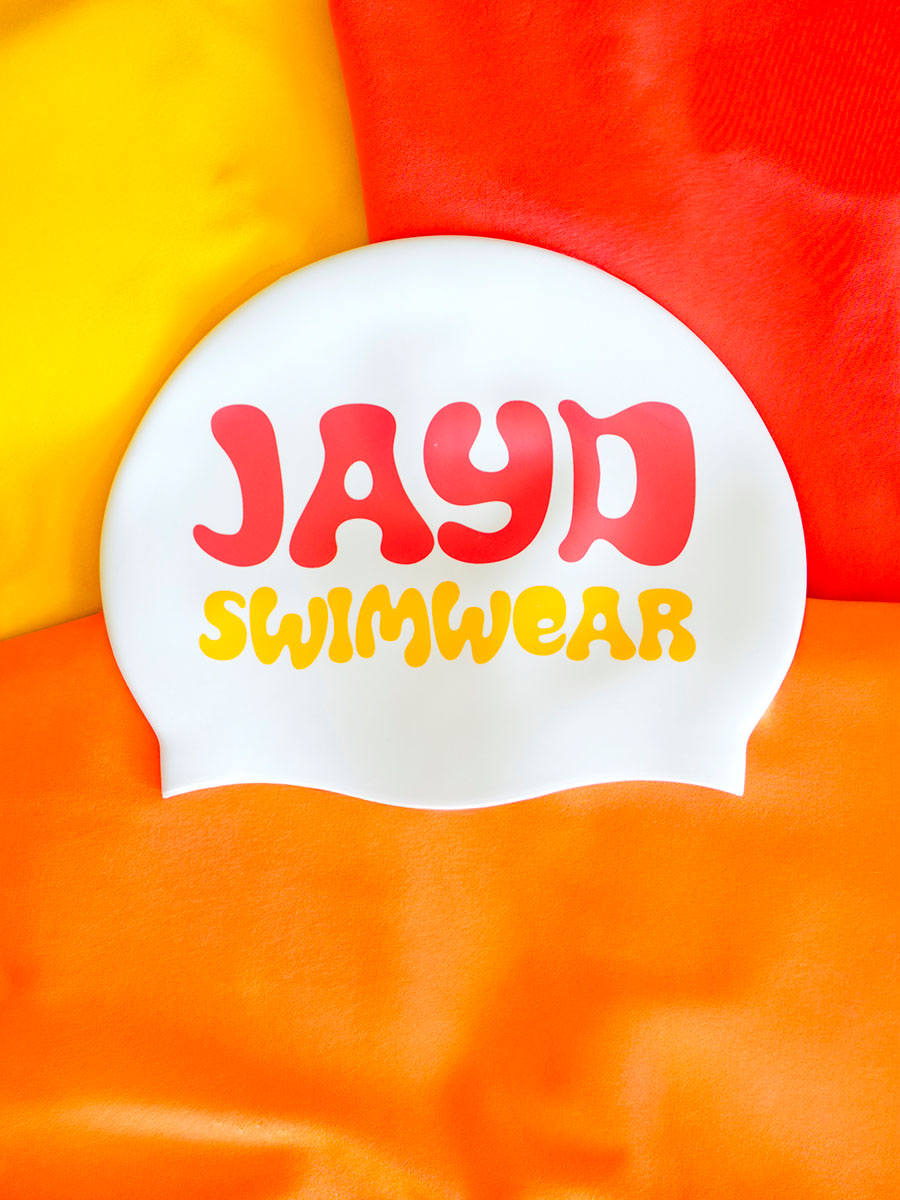 White swim cap with 'JAYD Swimwear' text on a colorful background