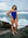 Open water swimmer Madi Armstrong standing on a rock at the beack with waves breaking behind her, wearing the JAYD Swimwear one piece swimsuit in cobalt blue with contrasting white shoulder straps.
